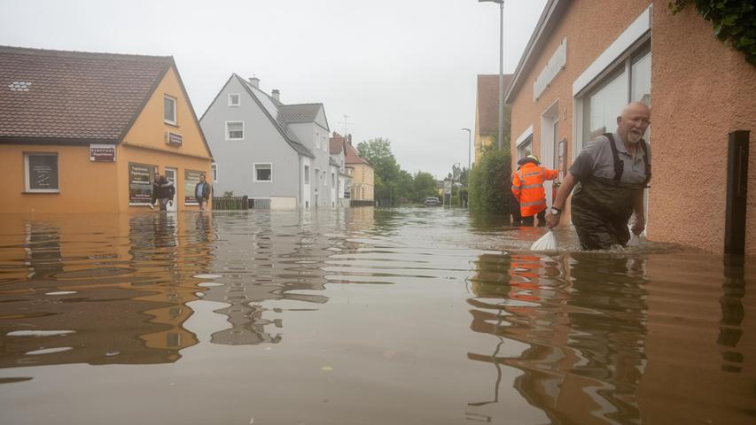 In einer überfluteten Straße in Wertingen (Kreis Dillingen) schleppt ein Mann Sandsäcke. Nach dem Starkregen der letzten Tage kam es zu schweren Überschwemmungen in der Region. Auch hier wurde am Samstagabend der Katastophenfall ausgerufen.