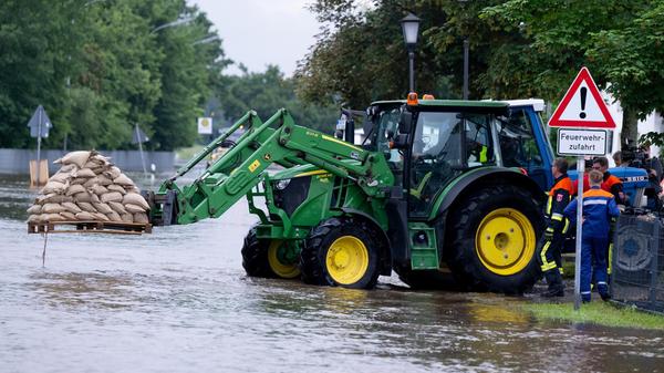 02.06.2024, Bayern, Reichertshofen: Helfer fahren mit einem Traktor Sandsäcke über eine überflutete Straße in Reichertshofen, einem Ort im Landkreis Pfaffenhofen an der Ilm.