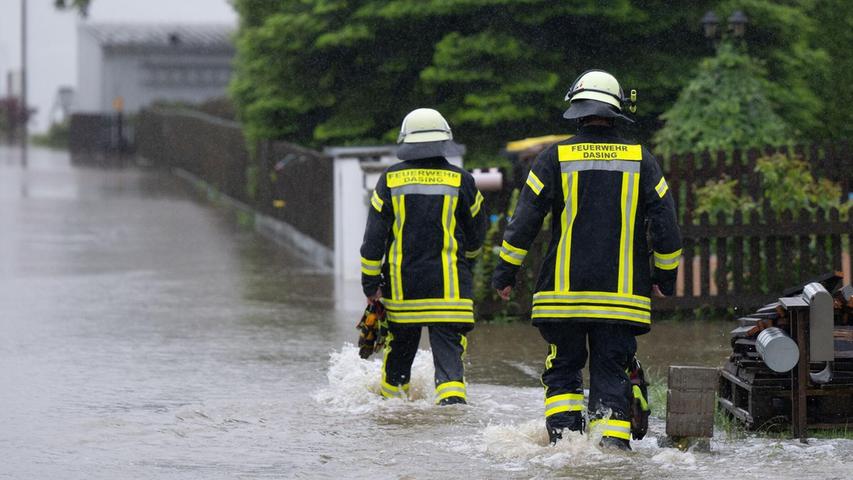 Feuerwehrleute gehen über eine überflutet Straße in Dasing.