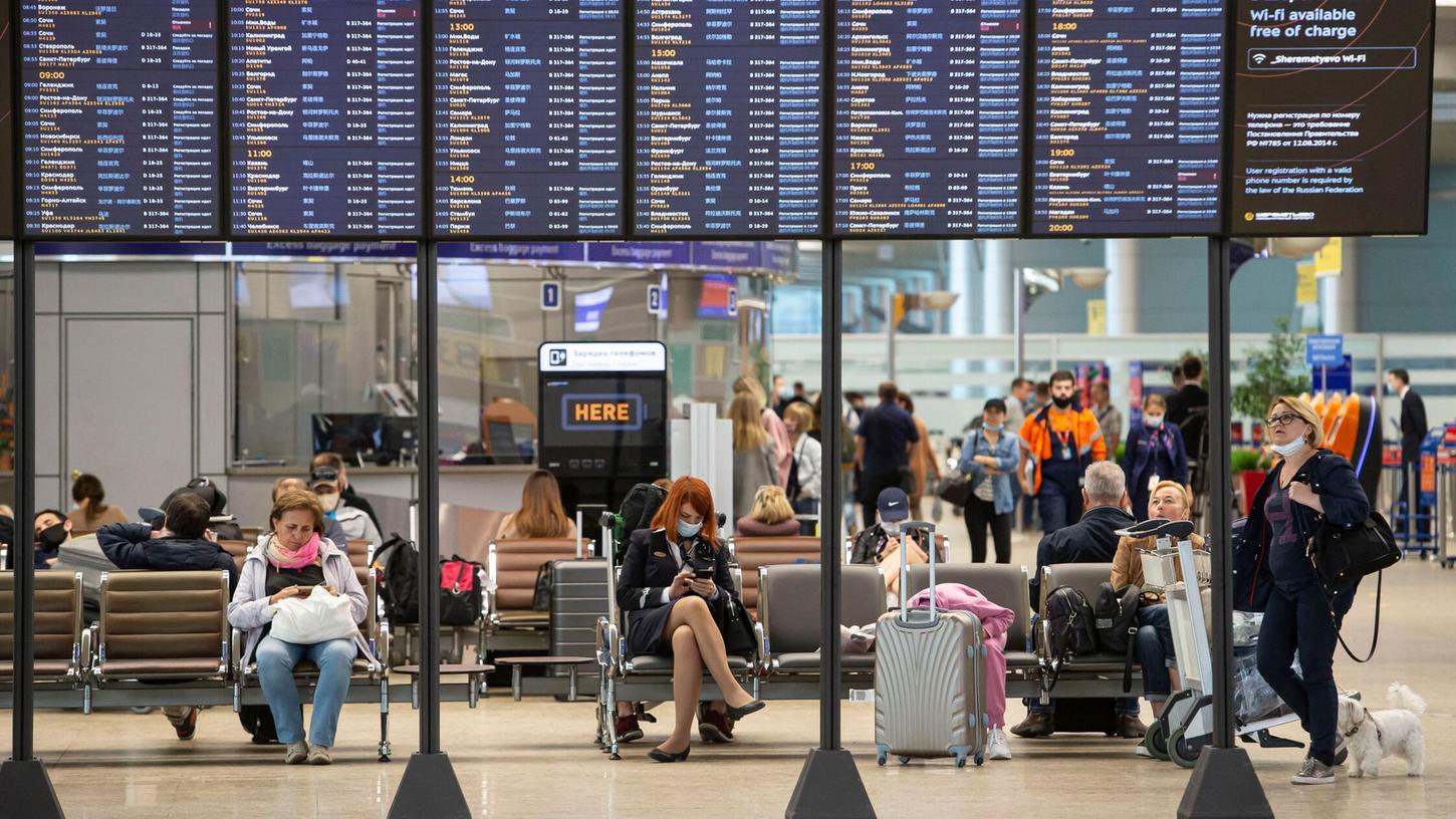 Passagiere sitzen auf dem internationalen Flughafen Scheremetjewo unter einer Fluginformationstafel. Passagiere sitzen auf dem internationalen Flughafen Scheremetjewo unter einer Fluginformationstafel.