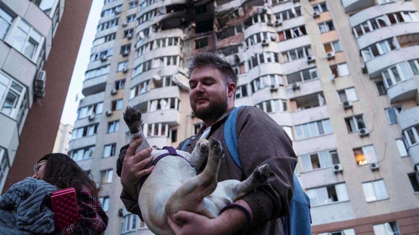 Ein Mann trägt seinen Hund vor einem mehrstöckigen Wohnhaus, das bei einem russischen Drohnenangriff auf Kiew, Ukraine, beschädigt wurde. Ein Mann trägt seinen Hund vor einem mehrstöckigen Wohnhaus, das bei einem russischen Drohnenangriff auf Kiew, Ukraine, beschädigt wurde.