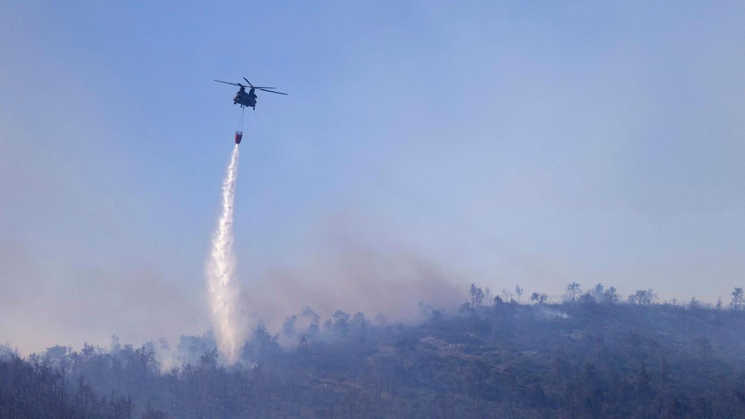 Ein Hubschrauber wirft Wasser auf einen Waldbrand im Norden Athens ab.