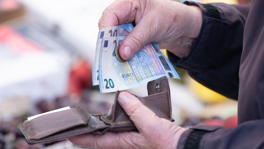 Eine Frau sortiert auf einem Wochenmarkt das Wechselgeld für ihre Einkäufe in ein Portemonnaie.