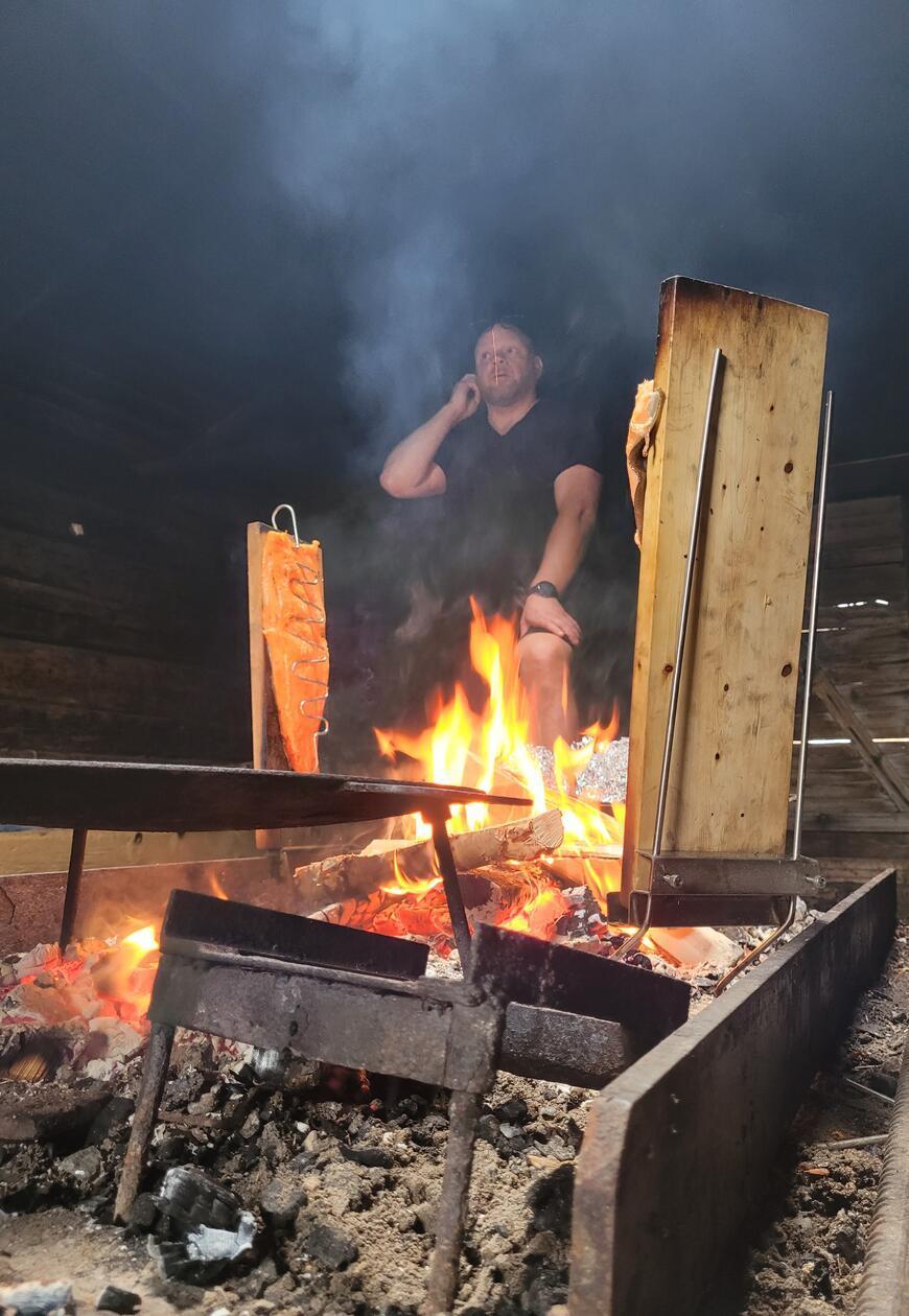 Die Räucherhütte steht der Gemeinschaft in Kukkolaforsen sowie auch deren urlaubenden Gästen offen. Es ist wie ein Gemeinschaftshaus, in dem sich auch im strengen Winter bei einem Plausch aufgewärmt wird. Jenni Rissanen, der Chef quasi, hat den frisch gefangenen Lachs auf Holzbretter gepinnt, das Feuer erledigt den Rest.