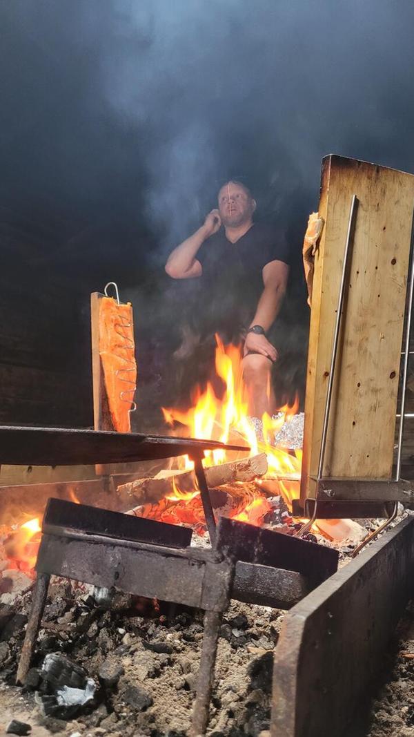 Die Räucherhütte steht der Gemeinschaft in Kukkolaforsen sowie auch deren urlaubenden Gästen offen. Es ist wie ein Gemeinschaftshaus, in dem sich auch im strengen Winter bei einem Plausch aufgewärmt wird. Jenni Rissanen, der Chef quasi, hat den frisch gefangenen Lachs auf Holzbretter gepinnt, das Feuer erledigt den Rest.