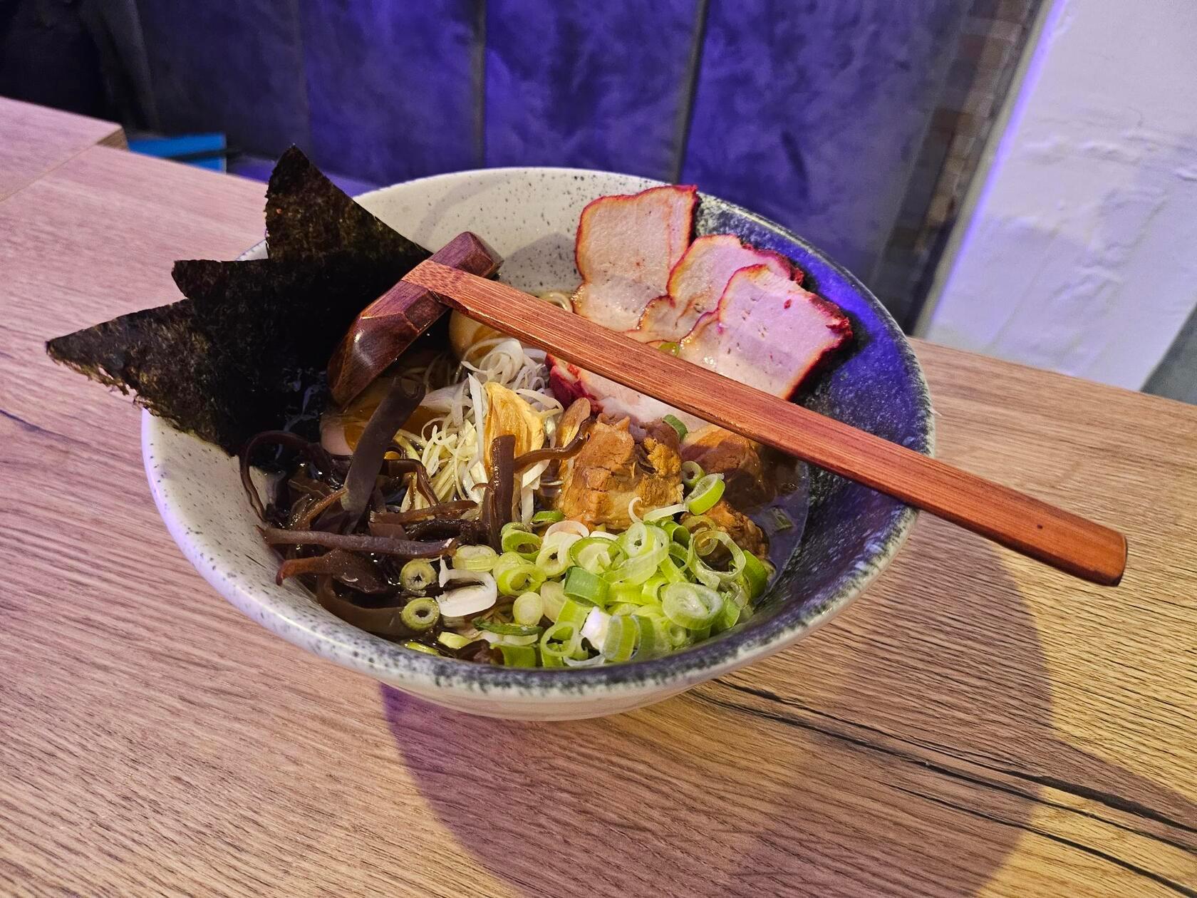 Tonkotsu-Ramen in Schweine- und Hühnerbrühe mit Nudeln, Schweine-Chashu, geschmortem Schweinebauch, Noriblättern, Frühlingszwiebeln, Morcheln, Porreestreifen, einem weich gekochtem Ei und Pfeffer.