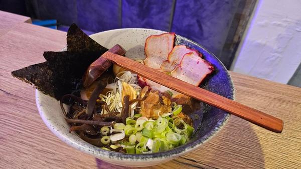 Tonkotsu-Ramen in Schweine- und Hühnerbrühe mit Nudeln, Schweine-Chashu, geschmortem Schweinebauch, Noriblättern, Frühlingszwiebeln, Morcheln, Porreestreifen, einem weich gekochtem Ei und Pfeffer.