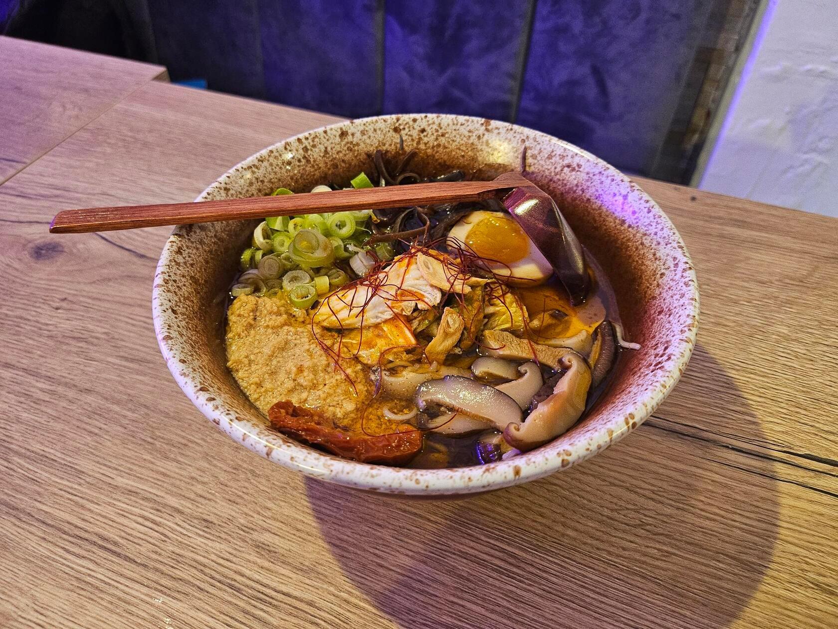 "Spicy Chicken"-Ramen in Hühnerbrühe mit Nudeln, gehacktem Maishuhn, Morcheln, getrockneten Tomaten, Kimchi, Shitake-Pilzen, Chili-Fäden, Frühlingszwiebeln, weich gekochtem Ei und Chili-Öl.