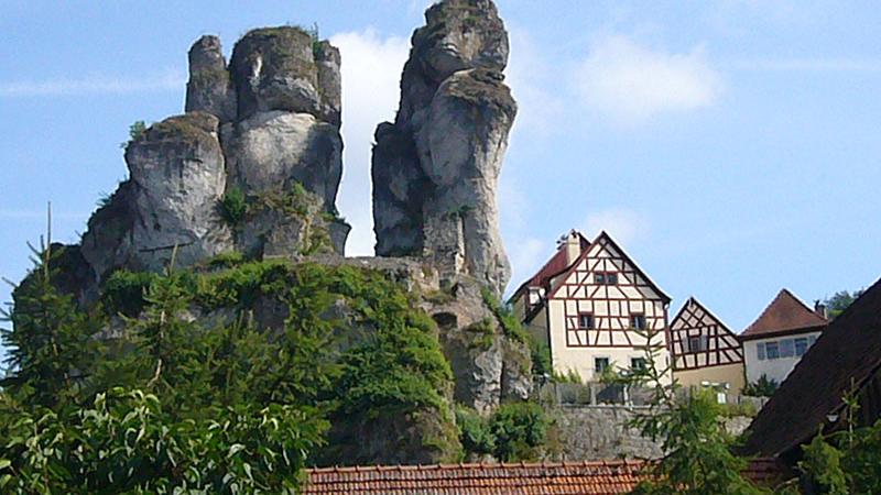 Wie versteinerte Riesen überragen die Felsen das fränkische Dörfchen Tüchersfeld. Die Fachwerkhäuser und Gehöfte schmiegen sich an die schroffen Steine, die aus dem Ur-Meer der Jurazeit stammen. Heute sind sie nicht nur ein markantes Wahrzeichen, sondern auch Ausgangspunkt und Ziel für Wanderungen. Die bizarren Formationen sind außerdem ein Abenteuerspielplatz für Bergsteiger.  