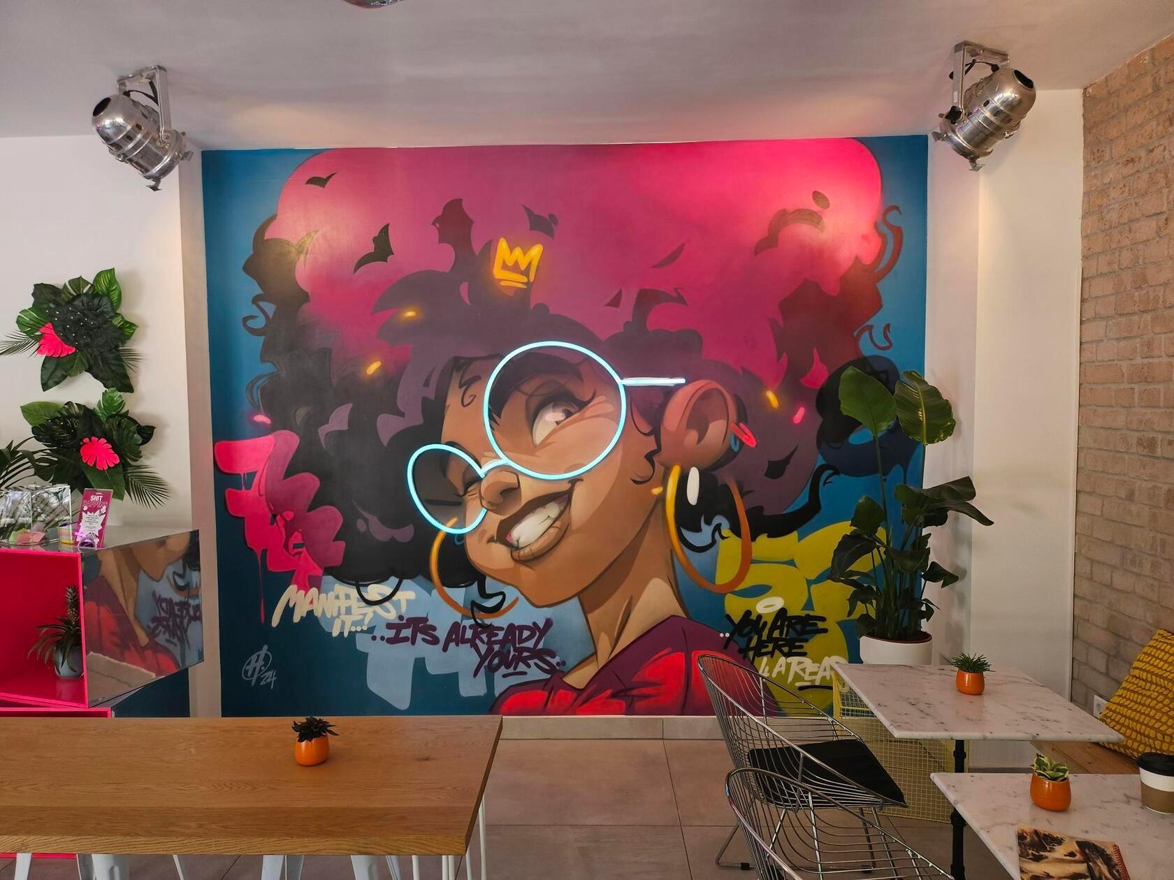 An der Rückwand des Restaurants prangt ein großes Graffiti. Der Künstler dahinter ist kein Geringerer als Hombre Suk. Ein Highlight - wortwörtlich - im Graffiti ist die leuchtende Brille, diese haben die Atlis selbst gestaltet und in das Kunstwerk eingebaut.