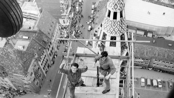 "Erregende Minuten über St. Lorenz": diese Aufnahme der eingerüsteten Turmspitze gelang unserer Fotografin Gertrud Gerardi im Mai 1959 durch die geöffnete Tür eines Helikopters der US-Armee. Er war vom Hans-Sachs-Platz gestartet, um die goldene Turmzierde, einen Stern mit Engel, zur Spitze des 81 Meter hohen Südturms der Lorenzkirche zu befördern, wo sie sodann montiert wurde und sich heute noch dreht. Der Einsatz des damals noch ungewöhnlichen Fluggeräts zog zahlreiche Nürnberger auf die Straßen der Altstadt, von wo sie das zehnminütige, aufregende Ringen von Besatzung und Handwerkern gegen den starken Wind beobachteten.