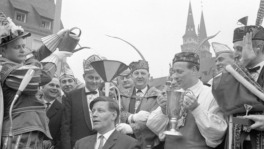 In banger Erwartung einer kalten Dusche saß Helmut Schmidt im Februar 1966 inmitten des närrischen Treibens auf dem Hauptmarkt. Der bekannte Humorist Herbert Hisel ließ als Faschingsprinz Herbertla I. mit einer Gießkanne „Weisheit“ in den roten Trichter fließen. Zum ersten Mal wurde die höchste Nürnberger Faschingsauszeichnung verliehen: der Goldene Nürnberger Trichter. In Vertretung für seinen erkrankten Parteigenossen Fritz Erler nahm der damalige SPD-Bundestagsabgeordnete Helmut Schmidt die Eintrichterung entgegen. Als späterer Bundeskanzler wurde er selbst sehr einflussreich. In banger Erwartung einer kalten Dusche saß Helmut Schmidt im Februar 1966 inmitten des närrischen Treibens auf dem Hauptmarkt. Der bekannte Humorist Herbert Hisel ließ als Faschingsprinz Herbertla I. mit einer Gießkanne „Weisheit“ in den roten Trichter fließen. Zum ersten Mal wurde die höchste Nürnberger Faschingsauszeichnung verliehen: der Goldene Nürnberger Trichter. In Vertretung für seinen erkrankten Parteigenossen Fritz Erler nahm der damalige SPD-Bundestagsabgeordnete Helmut Schmidt die Eintrichterung entgegen. Als späterer Bundeskanzler wurde er selbst sehr einflussreich.