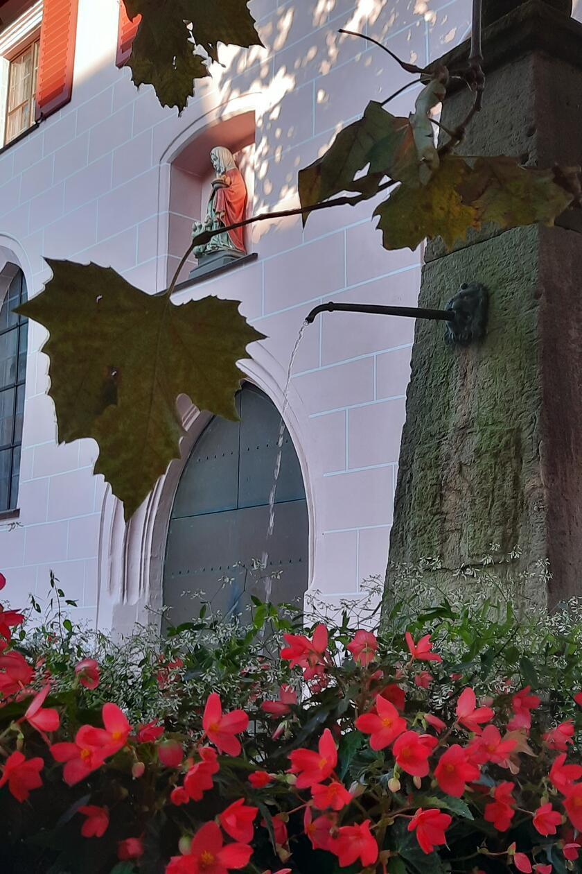 Brunnen im herbstlichen Abendlicht vor der Hersbrucker Spitalkirche mit Skulptur der Heiligen Elisabeth über dem Eingangsportal.