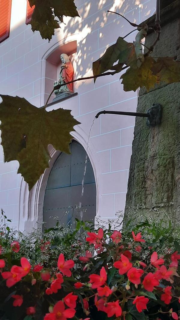 Brunnen im herbstlichen Abendlicht vor der Hersbrucker Spitalkirche mit Skulptur der Heiligen Elisabeth über dem Eingangsportal.
