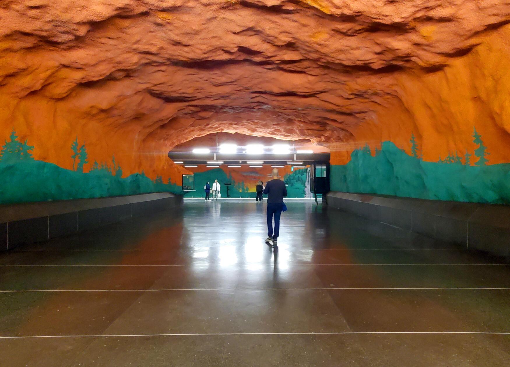 Station Solna Centrum - eine grün-rote Farbenexplosion: Das riesige Gemälde zeigt einen rot-orangenen Sonnenuntergang über dem Grün der schwedischen Wälder. Die Künstler Karl-Olov Björk und Anders Åberg haben zusätzlich Hunderte von kleine Zeichnungen an die Wände gemalt, die wichtige Themen aus dem Alltag zeigen, darunter auch manch Amüsantes.