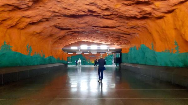 Station Solna Centrum - eine grün-rote Farbenexplosion: Das riesige Gemälde zeigt einen rot-orangenen Sonnenuntergang über dem Grün der schwedischen Wälder. Die Künstler Karl-Olov Björk und Anders Åberg haben zusätzlich Hunderte von kleine Zeichnungen an die Wände gemalt, die wichtige Themen aus dem Alltag zeigen, darunter auch manch Amüsantes.