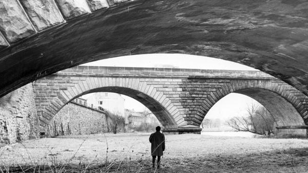 An der Stadtgrenze zwischen Nürnberg und Fürth steht im Februar 1962 ein Mann im Flussbett und blickt auf die Bögen des Dooser Brückkanals. Eine malerische Umgebung. Doch aufgrund der Verkehrsplanung verschwand sie kurz nach der Entstehung dieser Aufnahme. Noch im Lauf der 60er Jahre wurden beide abgebildeten Brücken abgerissen und eine Schnellstraße in die Trasse des alten Ludwig-Donau-Main-Kanals gebaut. Stünde man heute an dieser Stelle, so wäre man direkt unterhalb der Kurgartenbrücke mitten auf dem Frankenschnellweg. Bis heute ein umstrittenes Verkehrsprojekt, dessen weiterer Ausbau kontrovers diskutiert wird.