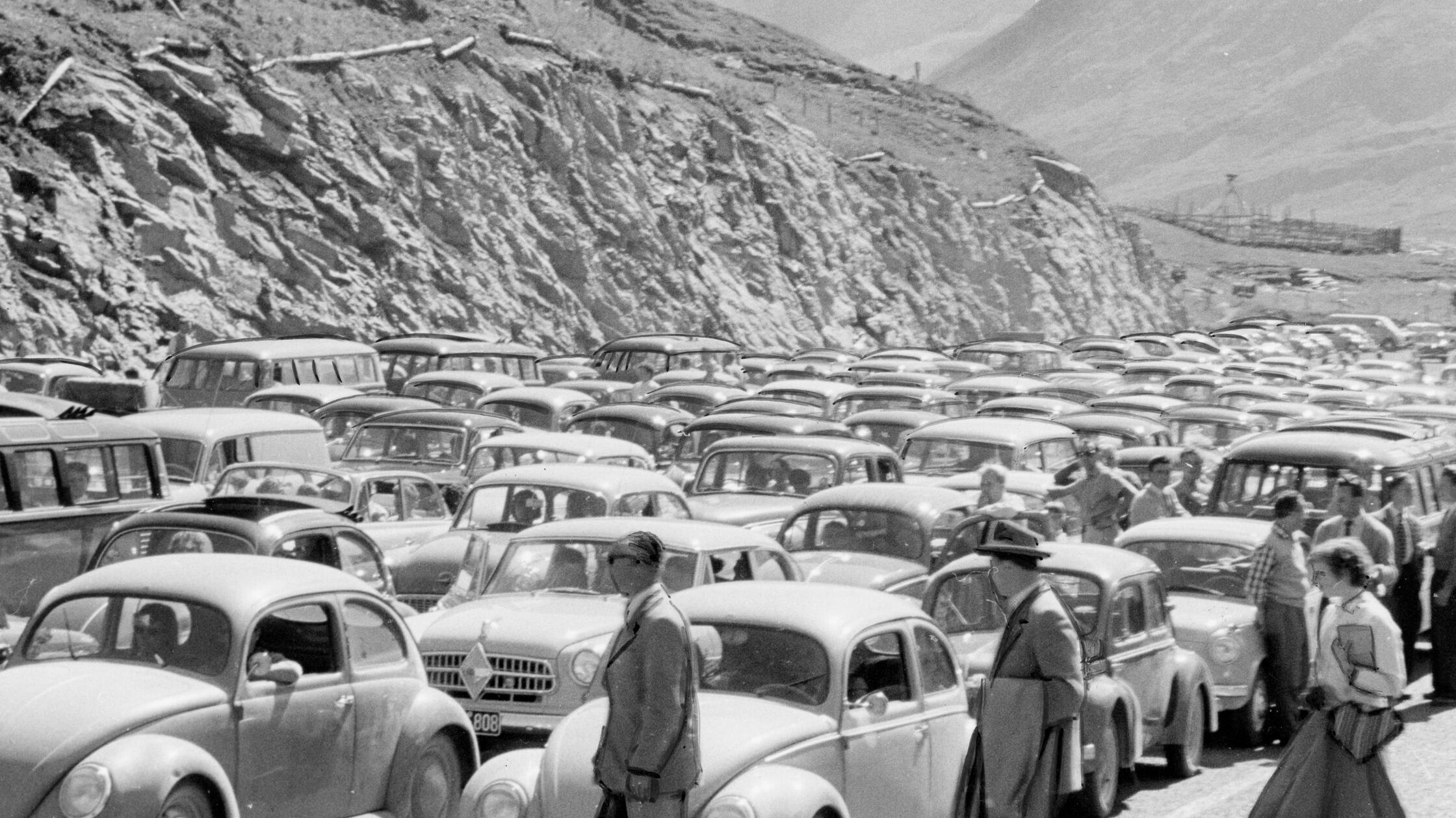 Letzte Sommertage für einen Kurztrip zu nutzen, ist eine schöne Idee. Statt am ersehnten Ort verbringen Reiselustige jedoch oft einen großen Teil ihrer Freizeit inmitten einer Blechlawine. So auch unser Fotograf, der im September 1956 an der Großglockner Hochalpenstraße in einem Meer aus stehenden Fahrzeugen über drei Stunden lang Gelegenheit hatte, Aufnahmen wie diese zu machen. Bereits ab Mitte der 1950er Jahre wurden Staus an beliebten Reisetagen zunehmend alltäglich. Anders als heute wartete man damals jedoch ohne Klimaanlage und Unterhaltungselektronik, dafür - wie auf unserem Bild zu sehen - in stilvoller Garderobe.
