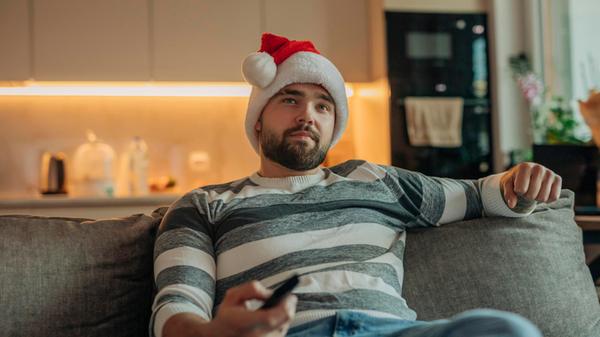 Young man wearing Santa hat and watching TV in liv