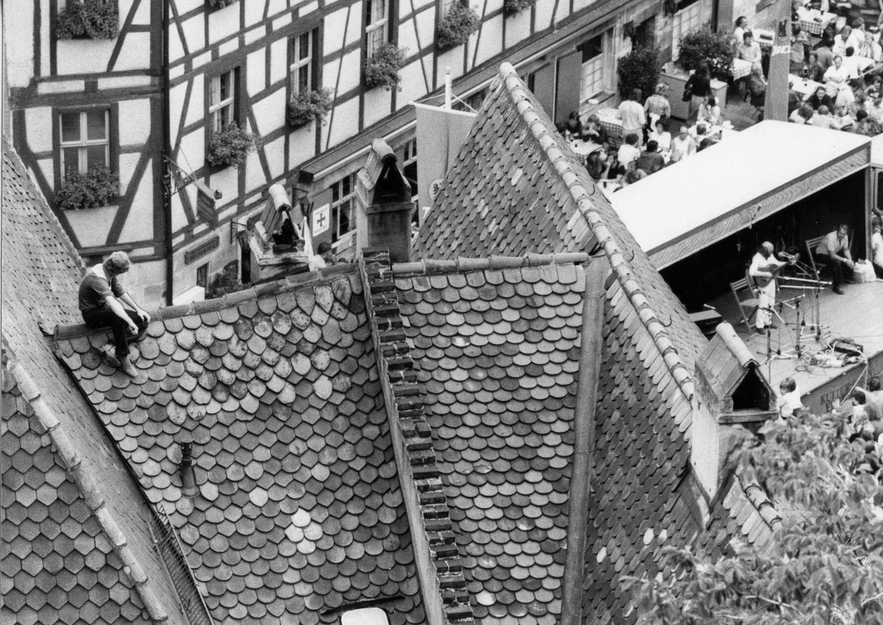 Hoch hinaus wollte der Herr links in unserem Foto: Beim Bardentreffen 1979 sicherte er sich einen möglicherweise nicht ganz den Sicherheitsstandards entsprechenden Logenplatz, indem er ein Dach in der Altstadt bestieg. Von dort hatte er gute und unverstellbare Sicht auf die Bühne am Tiergärtnertorplatz, damals eine der Hauptspielstätten des Nürnberger Musikfestes. Knapp 70 Liedermacher hatte die Stadt damals zum vierten Bardentreffen eingeladen, weit mehr waren jedoch zusätzlich und auf eigene Rechnung angereist und musizierten auf den Straßen und auch in den Kneipen im Sebalder und im Lorenzer Viertel.