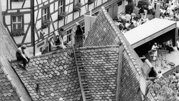 Hoch hinaus wollte der Herr links in unserem Foto: Beim Bardentreffen 1979 sicherte er sich einen möglicherweise nicht ganz den Sicherheitsstandards entsprechenden Logenplatz, indem er ein Dach in der Altstadt bestieg. Von dort hatte er gute und unverstellbare Sicht auf die Bühne am Tiergärtnertorplatz, damals eine der Hauptspielstätten des Nürnberger Musikfestes. Knapp 70 Liedermacher hatte die Stadt damals zum vierten Bardentreffen eingeladen, weit mehr waren jedoch zusätzlich und auf eigene Rechnung angereist und musizierten auf den Straßen und auch in den Kneipen im Sebalder und im Lorenzer Viertel.