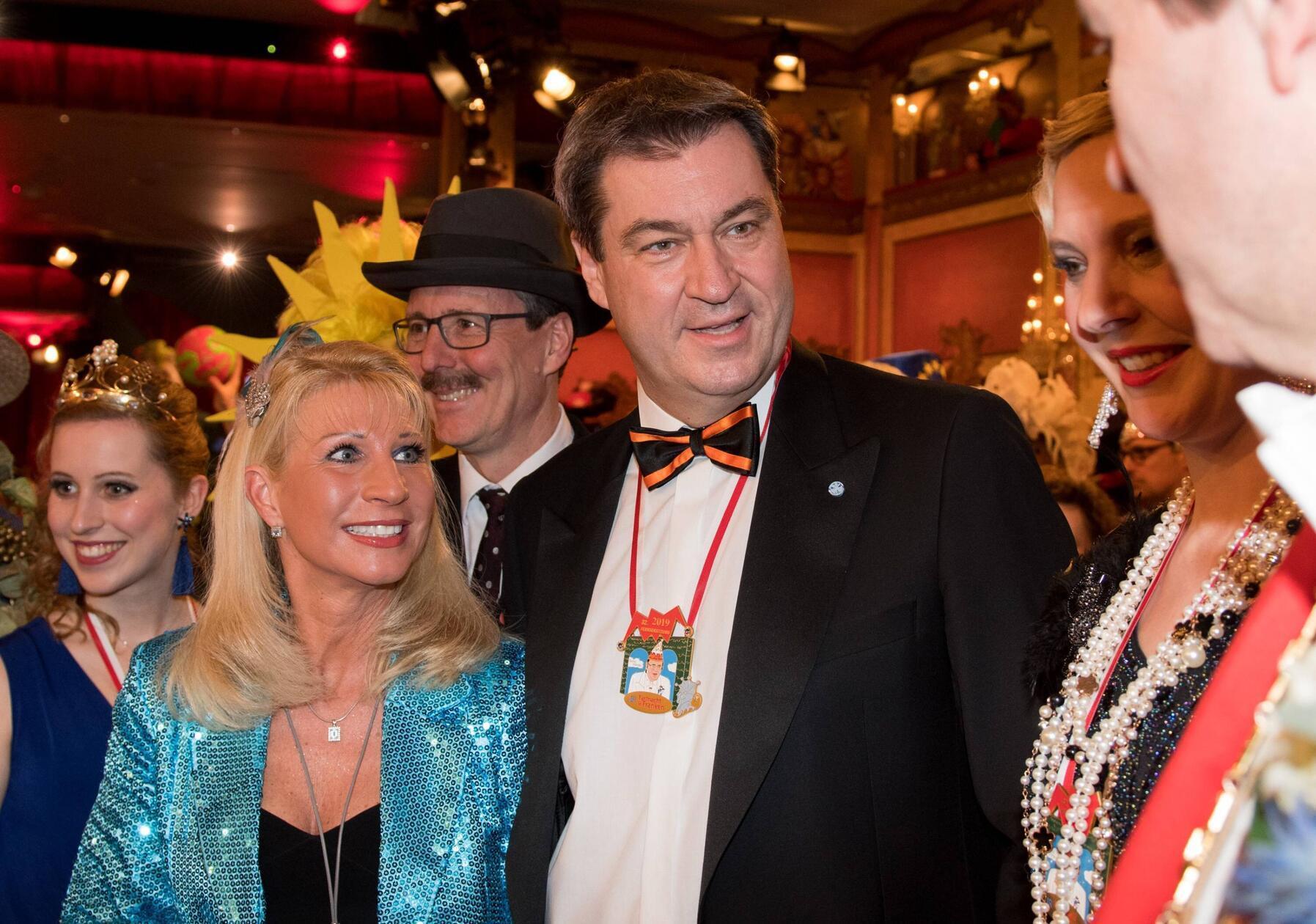 Auch 2019 bleibt Söders "Kostüm" eher einfallslos - immerhin lässt sich das schimmernd blaue Kleid seiner Frau als Meerjungfrau-Versuch interpretieren.