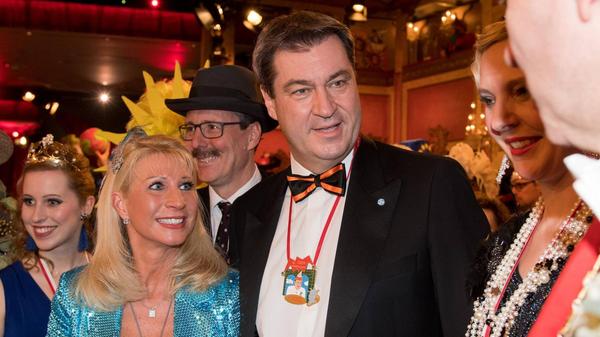 Auch 2019 bleibt Söders "Kostüm" eher einfallslos - immerhin lässt sich das schimmernd blaue Kleid seiner Frau als Meerjungfrau-Versuch interpretieren.