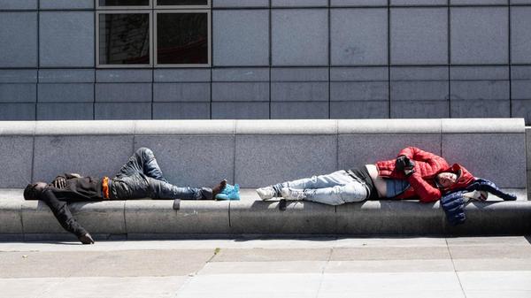 Two men sleep on a bench after Mayor London Breed