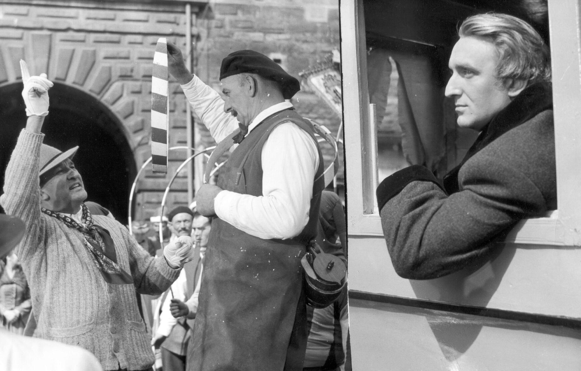 „What is happening here?“, fragt Richard Wagner aus einer Kutsche, die über den von buntem Treiben belebten Tiergärtnertorplatz fährt. Der Kutscher: „Oh, today is Häns-Sächs-Day, the most important day of Nuremberg“. „Oh yes, the shoemaker and poet!“, ruft da Wagner, und wird sogleich zu den „Meistersingern von Nürnberg“ inspiriert. Wir befinden uns im Jahr 1954 bei den Dreharbeiten für den Hollywood-Film "Frauen um Richard Wagner". Hauptdarsteller Alan Badel blickt hier ernst aus der Kutsche, während ein Herr vom "Verein Nürnberger Büttnertanz" Regisseur William Dieterle (li.) die Kunst des Reifenschwingens erklärt.