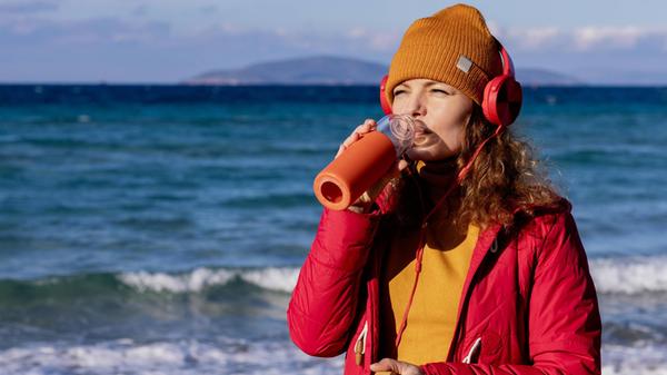 young woman with headphones drinking water by the