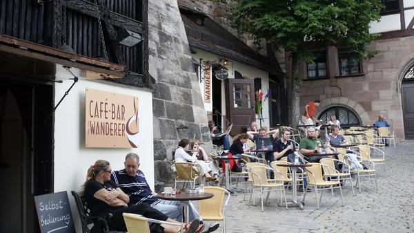 Bevor die Sommersaison des Café Wanderers zum 1. Mai offiziell startet, nehmen Nürnbergerinnen und Nürnberger Platz am Boden, um die Sonnenstrahlen inmitten der Altstadt zu genießen. Aktuell hat das Café Dienstag bis Sonntag von 10 Uhr bis 19 Uhr geöffnet, ab Mai können Interessierte das Lokal täglich von 10 Uhr bis 0 Uhr besuchen und im bestuhlten Außenbereich Platz nehmen.