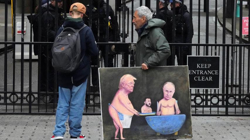 Ein Künstler geht in London mit einem Gemälde von Trump, Selenskyj und Putin am Tag der Ukraine-Gespräche vor den Toren der Downing Street 10 entlang. Ein Künstler geht in London mit einem Gemälde von Trump, Selenskyj und Putin am Tag der Ukraine-Gespräche vor den Toren der Downing Street 10 entlang.