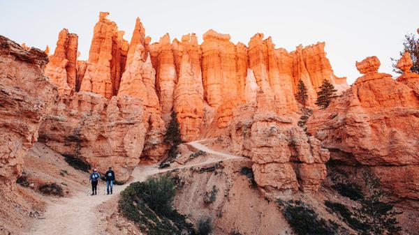 Hikers on a canyon trail with tall, orange rock sp