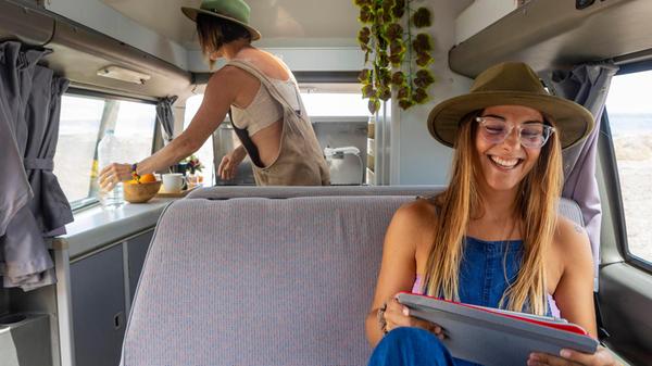 A lesbian couple relax inside a camper. One prepar