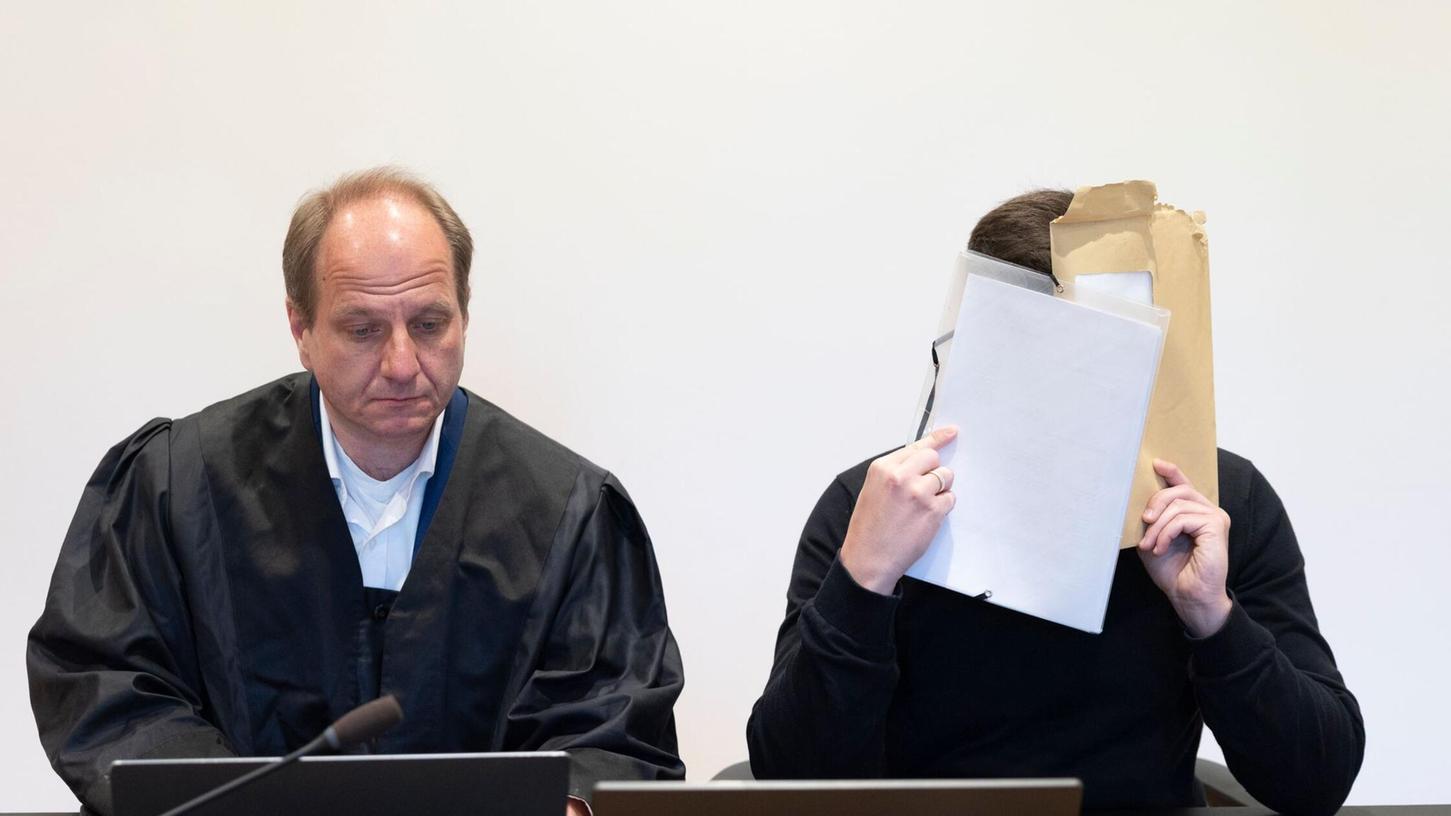Der angeklagte Aushilfslehrer (r) sitzt neben seinem Rechtsanwalt Marc Wandt im Sitzungssaal des Amtsgerichts in Haßfurt, in dem die Hauptverhandlung gegen ihn beginnt, und verdeckt sein Gesicht. Der Aushilfslehrer soll in Unterfranken nackte Grundschulkinder in Umkleidekabinen eines Schwimmbades gefilmt haben. Der angeklagte Aushilfslehrer (r) sitzt neben seinem Rechtsanwalt Marc Wandt im Sitzungssaal des Amtsgerichts in Haßfurt, in dem die Hauptverhandlung gegen ihn beginnt, und verdeckt sein Gesicht. Der Aushilfslehrer soll in Unterfranken nackte Grundschulkinder in Umkleidekabinen eines Schwimmbades gefilmt haben.