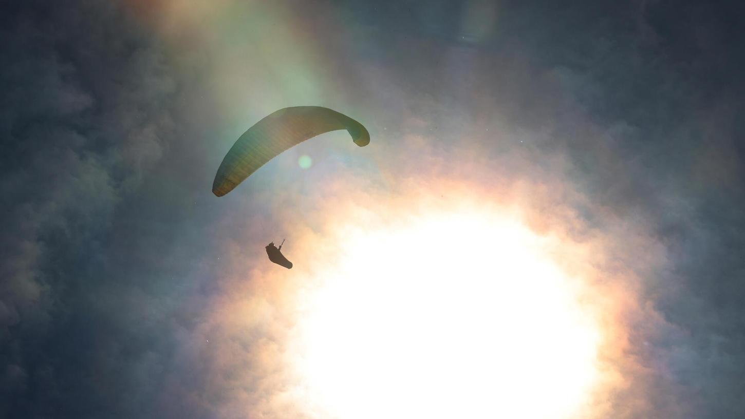 Bayern, Buching: Ein Gleitschirmflieger gleitet vor der Sonne am wolkenlosen Himmel über den Buchenberg. Bayern, Buching: Ein Gleitschirmflieger gleitet vor der Sonne am wolkenlosen Himmel über den Buchenberg.