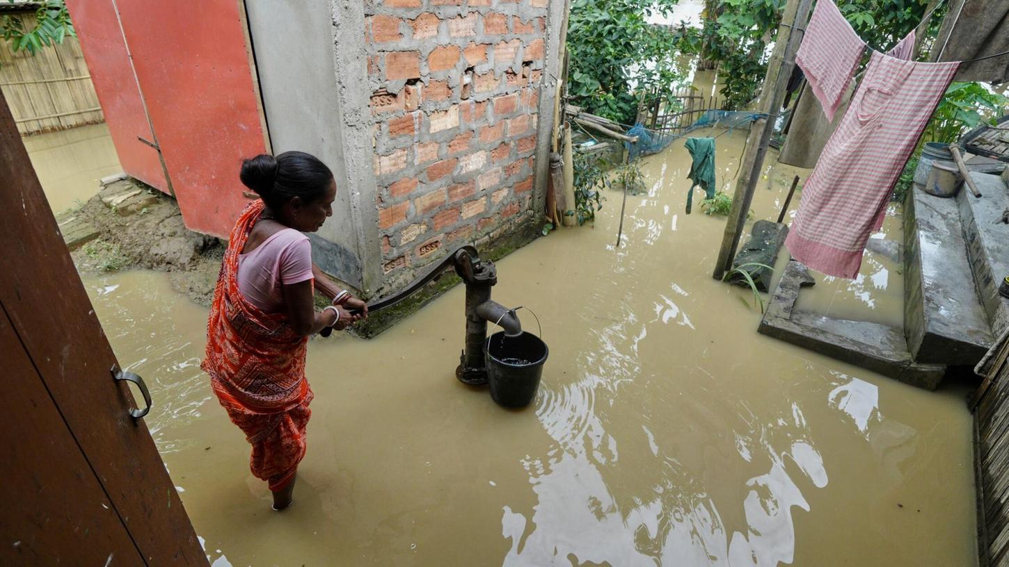 Eine Frau versucht in der überfluteten Umgebung ihres Hauses, Wasser zu sammeln. Eine Frau versucht in der überfluteten Umgebung ihres Hauses, Wasser zu sammeln.