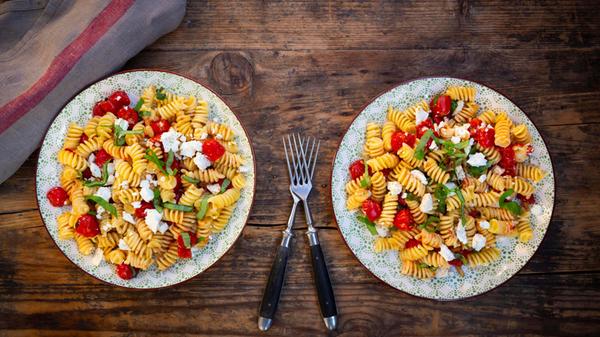 Two plates of pasta salad with tomatoes, feta chee