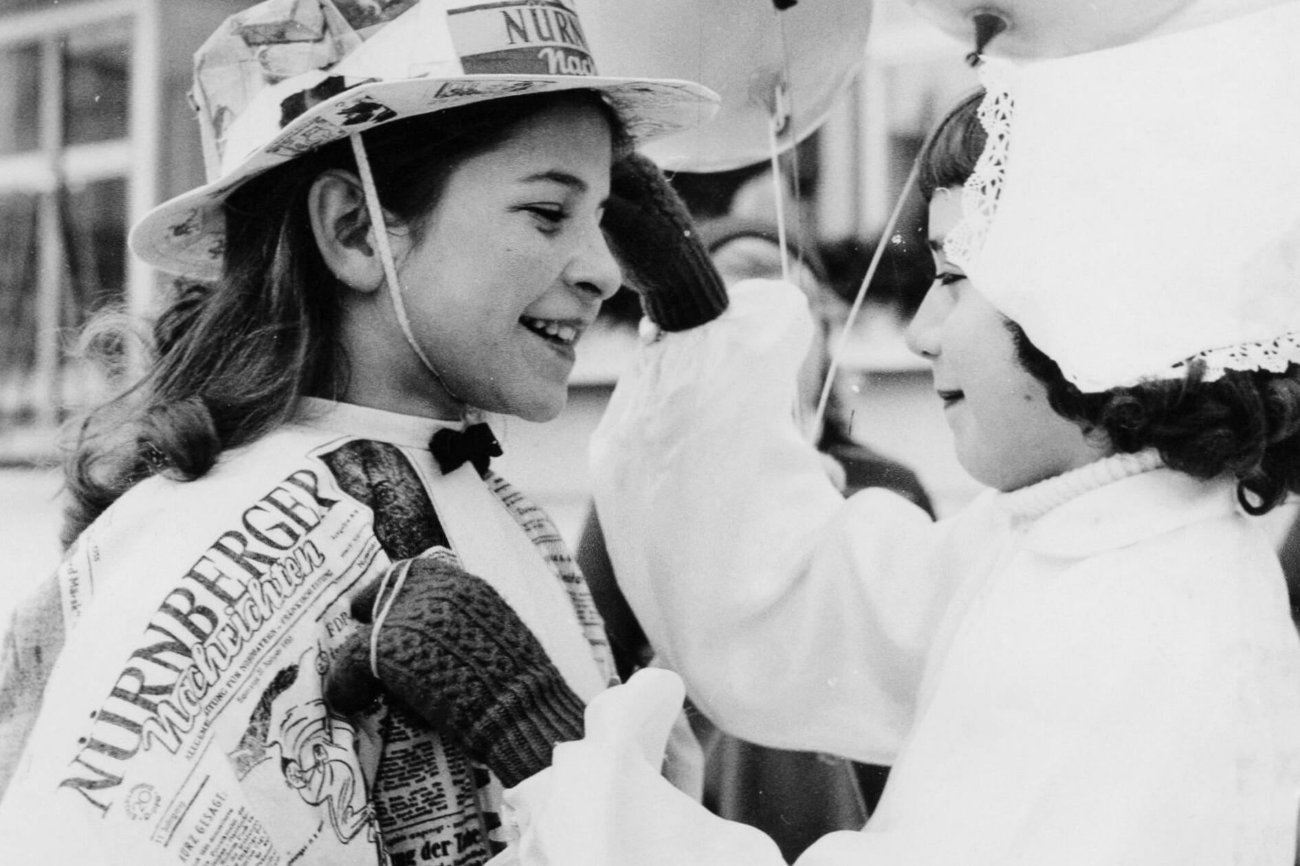 Beim Eisfasching im Januar 1955 wird ein Mädchen mit einem Kostüm aus Zeitungspapier der Nürnberger Nachrichten von einer kleinen „Holländerin“ bestaunt. Wo heute das Einkaufszentrum Mercado in Nürnberg steht, war bis zum Jahr 2001 das Linde-Eisstadion. Jeden Mittwoch in der Faschingszeit durften Kinder dort kostümiert auf der Eisfläche herumsausen. Bei kleinen Wettbewerben, wie Eierlauf auf Schlittschuhen, konnten sie etwas Süßes gewinnen, und es gab natürlich auch eine Masken-Prämierung. Im Mittelpunkt des fröhlichen Treibens war stets ein Schlittschuhfahrer im Eisbärkostüm, gestellt vom Linde-Stadion selbst, der immer eine Schar Kinder an seinem zottigen Fell hinter sich herzog und sie geduldig auf seinem Rücken reiten ließ.