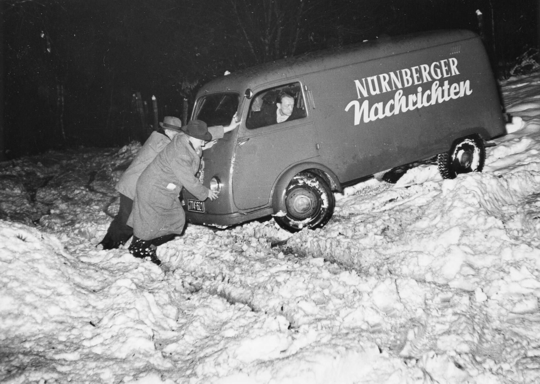 Wind und Wetter können bisweilen einer zuverlässigen Zeitungslieferung im Weg stehen. Dieses leidige Problem ist nicht neu, schon in den 1950er Jahren konnte es bei übermäßig harscher Witterung zu Schwierigkeiten bei der Zustellung kommen. Zum Glück hatte unser im Schnee steckengebliebener Zeitungsfahrer engagierte Helfer. Ob es seinerzeit gelang, ihn schnell aus seiner misslichen Lage zu befreien, entzieht sich unserer Kenntnis. Sein gleichmütig-resignierter Blick lässt jedoch erahnen, dass dies nicht sein erstes winterliches Erlebnis dieser Art war.