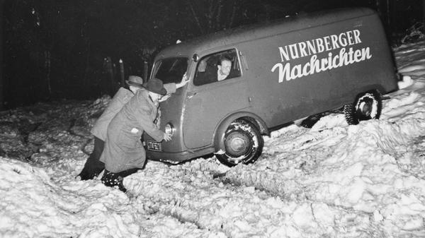 Wind und Wetter können bisweilen einer zuverlässigen Zeitungslieferung im Weg stehen. Dieses leidige Problem ist nicht neu, schon in den 1950er Jahren konnte es bei übermäßig harscher Witterung zu Schwierigkeiten bei der Zustellung kommen. Zum Glück hatte unser im Schnee steckengebliebener Zeitungsfahrer engagierte Helfer. Ob es seinerzeit gelang, ihn schnell aus seiner misslichen Lage zu befreien, entzieht sich unserer Kenntnis. Sein gleichmütig-resignierter Blick lässt jedoch erahnen, dass dies nicht sein erstes winterliches Erlebnis dieser Art war.