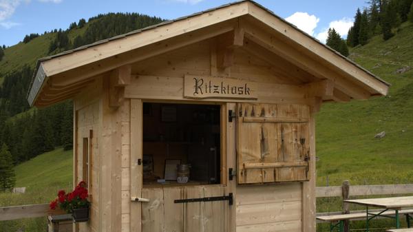 Der niedliche Kiosk neben der Alp Ritz enthält alle Produkte, die die Wirtschaft hergibt: Hobelkäse und Alpkäse, den sogenannen „Mutschli“-Käse, der vier Monate lang gereift ist, sowie Ziegenkäse und frische Milch. Außerdem gibt es Rindersalami und eine Auswahl an heißen und kalten Getränken – alles in Selbstbedienung
