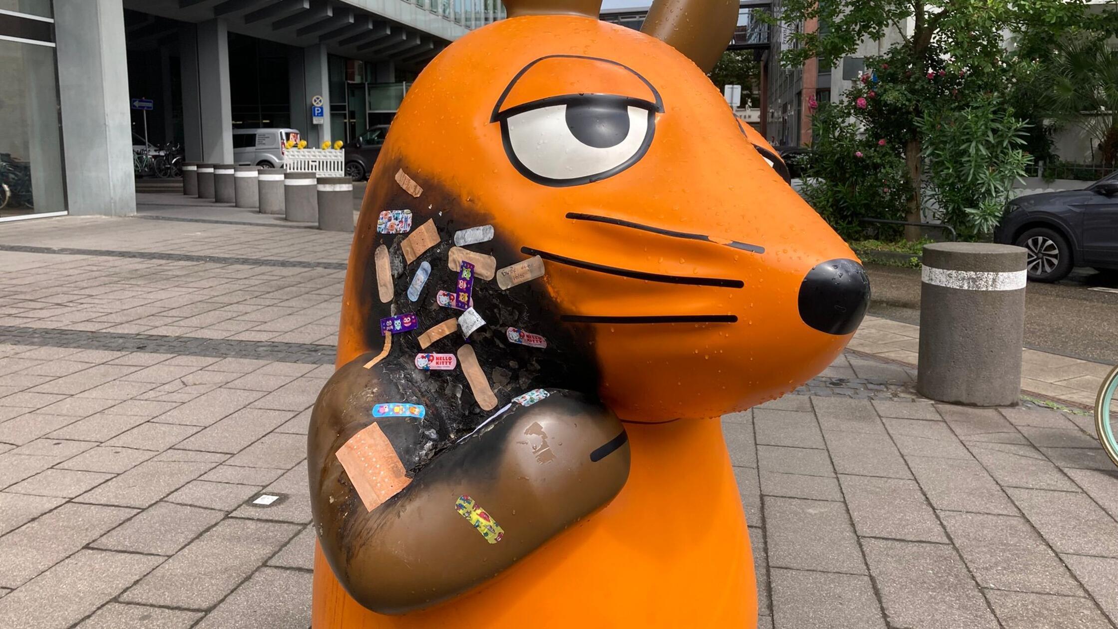 Angebrannte Maus-Figur wird mit Pflastern versorgt