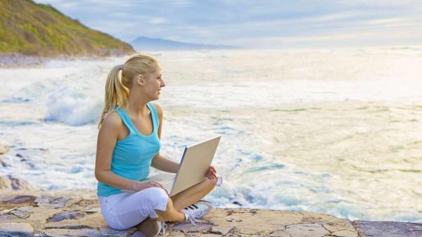 Beautiful young woman with laptop looking at ocean