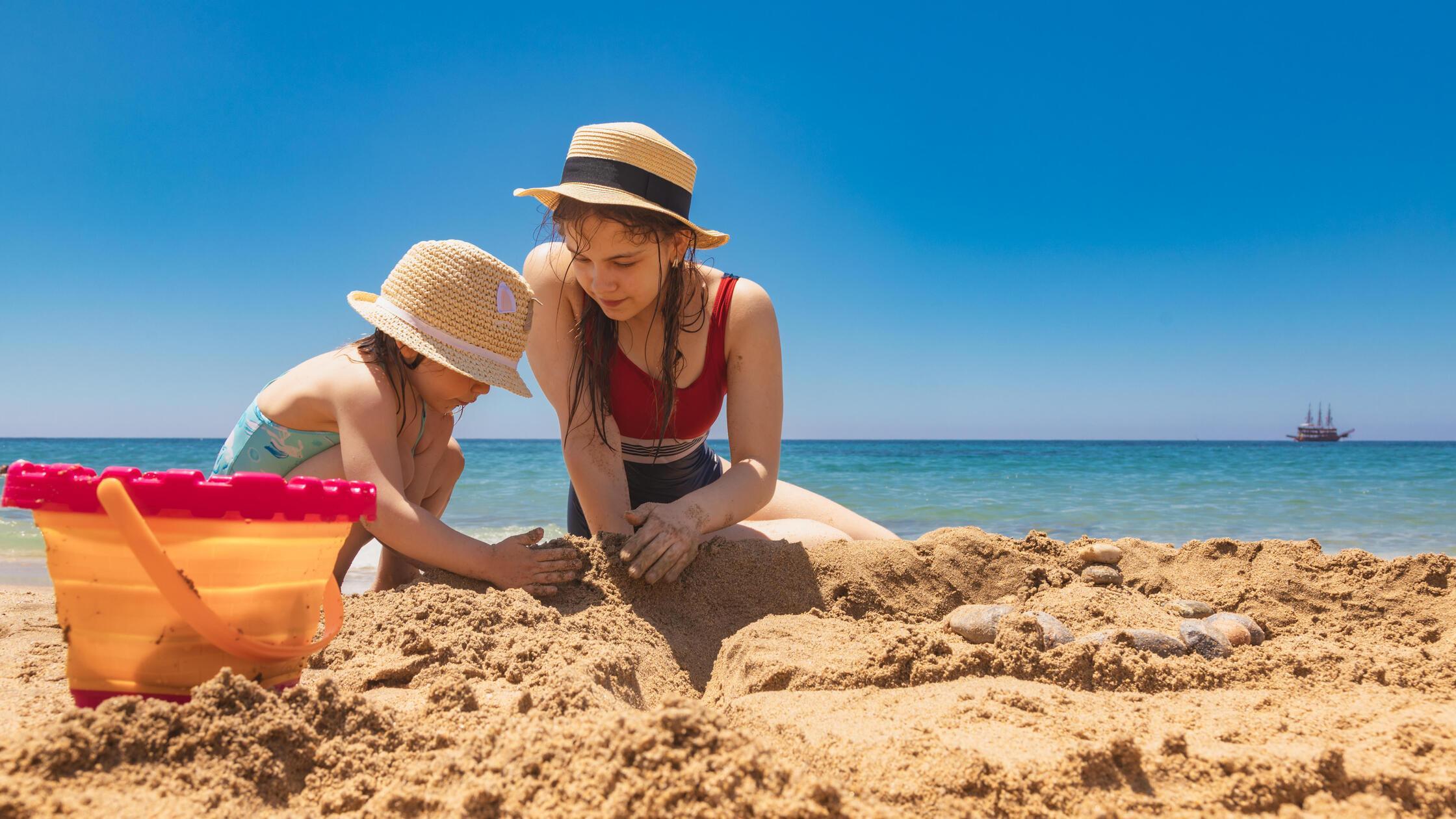 Schwestern mit Sonnenhüten bauen eine Sandburg am 