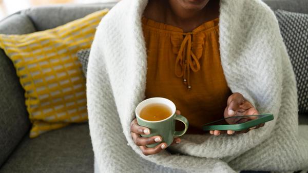 Smiling woman wrapped in blanket using smart phone