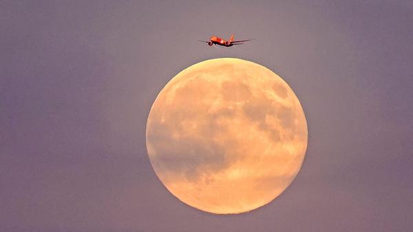 Ein Flugzeug fliegt vor dem Supermond am frühen Abend über Leipzig.