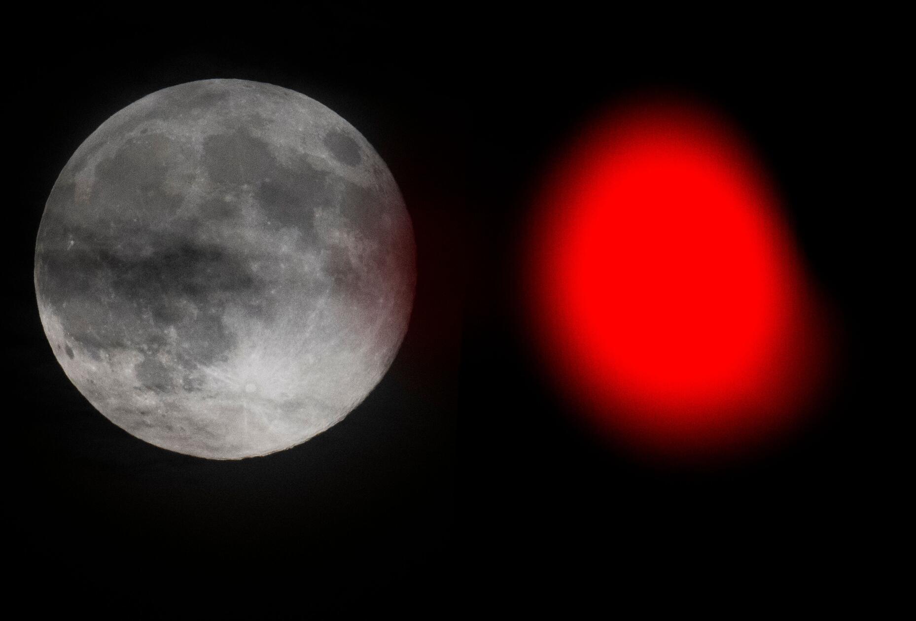 Der Vollmond steht neben einer roten Ampel am Himmel über Frankfurt.