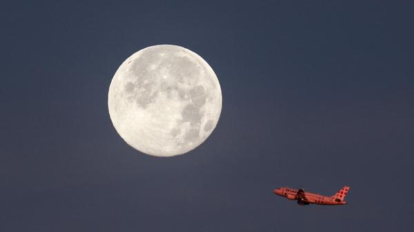 Ein Passagierflugzeug startet vom Airport in Hamburg und fliegt vor dem untergehenden Mond vorbei.