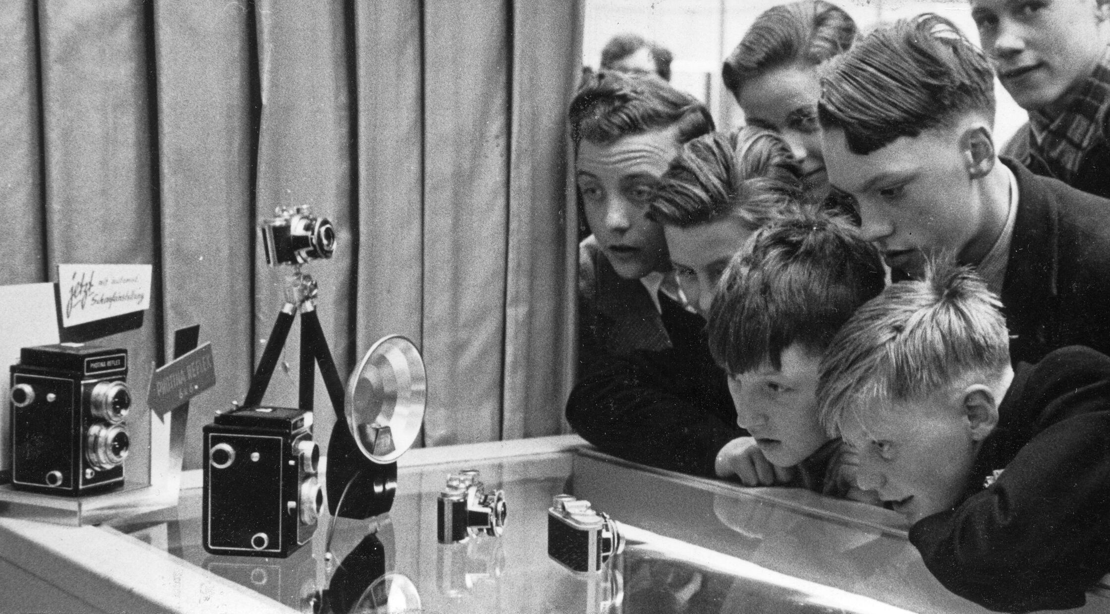 Wir schreiben das Jahr 1954 und befinden uns bei der vierten „Photo- und Kino-Ausstellung“, der „photokina“ in Köln. 176.000 Besucher wurden registriert, über 400 Firmen zeigten ihre neuen Entwicklungen. Interessenten, Aussteller und Importeure aus vielen Ländern fanden sich ein. Doch auch einige Nürnberger Firmen waren dabei. Auf unserem Bild bewundern einige Jungen verzückt die Photina Reflex-Kamera und die Photavit Kleinbildkamera aus den Bolta-Werken in Nürnberg. In ihre Gesichter, von denen es damals noch keine Selfies gab, steht die pure Begeisterung geschrieben.